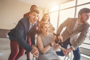 Unstoppable team! Four young cheerful business people in smart casual wear having fun while racing on office chairs and smiling